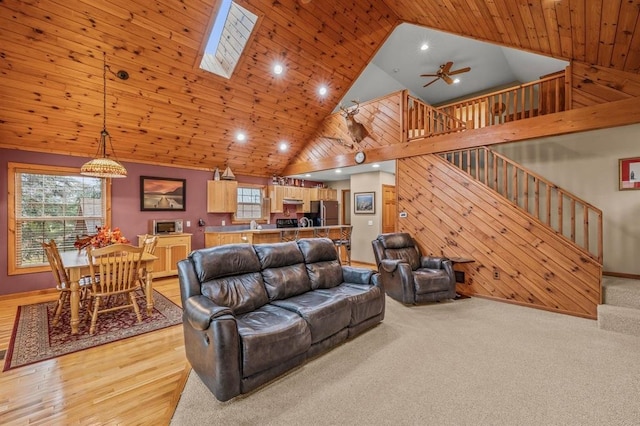 living room with light hardwood / wood-style flooring, wooden ceiling, a skylight, high vaulted ceiling, and ceiling fan