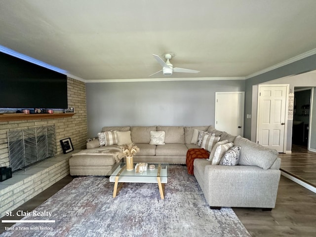 living room with a brick fireplace, ceiling fan, dark wood-type flooring, and ornamental molding