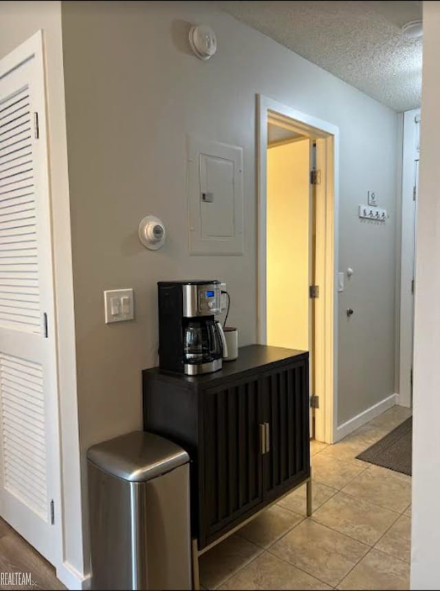 corridor with light tile patterned floors, a textured ceiling, and electric panel