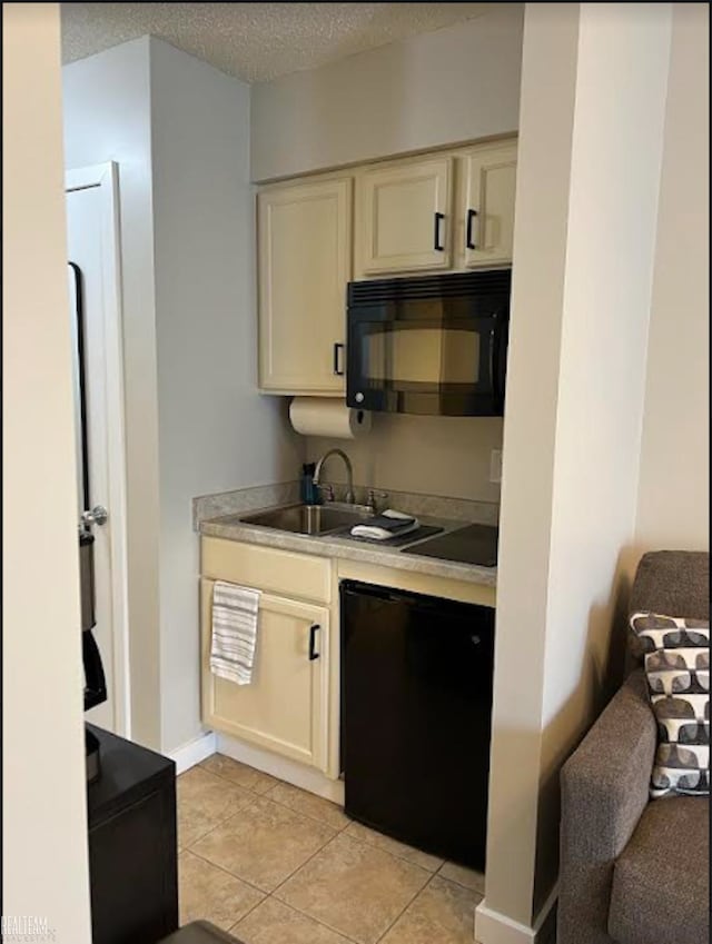 bar featuring cream cabinets, sink, black appliances, light tile patterned floors, and a textured ceiling