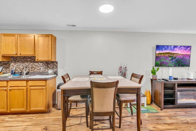 dining space with ornamental molding, sink, and light wood-type flooring