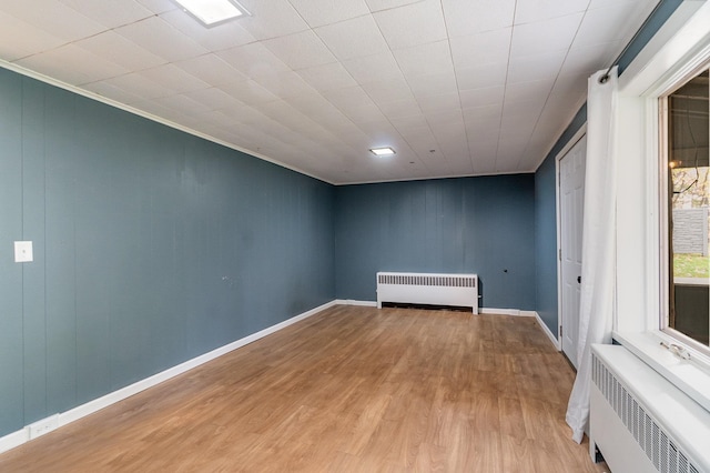 empty room with light hardwood / wood-style floors, ornamental molding, and radiator