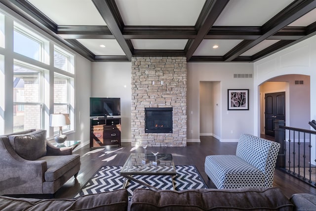 living room with a stone fireplace, beam ceiling, and dark wood-type flooring