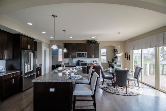 kitchen with stainless steel appliances, an island with sink, dark hardwood / wood-style floors, and hanging light fixtures