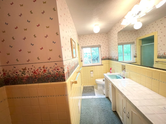 bathroom featuring a textured ceiling, vanity, tile walls, and toilet