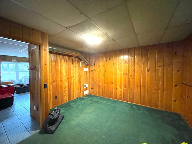 basement featuring carpet flooring, a paneled ceiling, and wooden walls