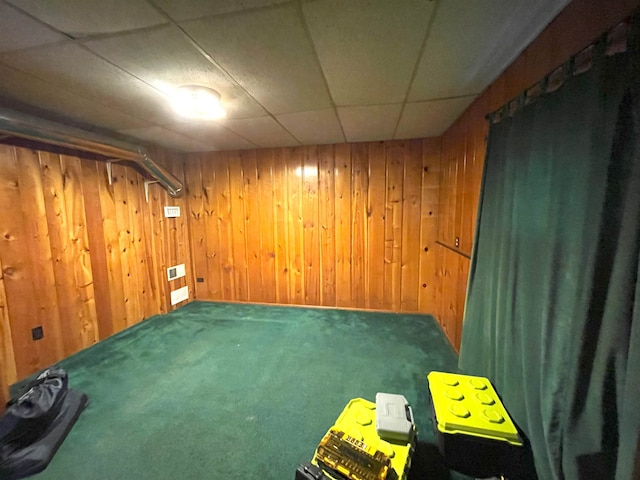 basement with carpet flooring, a drop ceiling, and wood walls