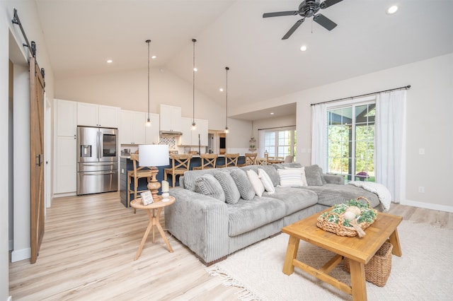 living room with a barn door, high vaulted ceiling, light hardwood / wood-style floors, and ceiling fan