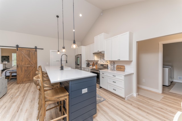 kitchen featuring a barn door, white cabinetry, stainless steel appliances, high vaulted ceiling, and a center island with sink