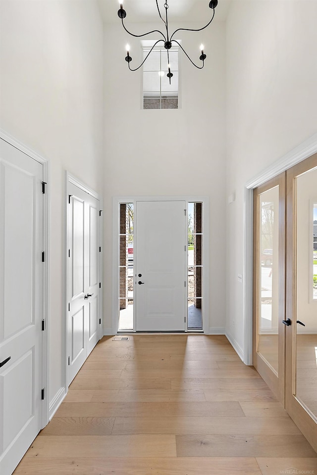 foyer with light hardwood / wood-style floors, french doors, a chandelier, and a high ceiling