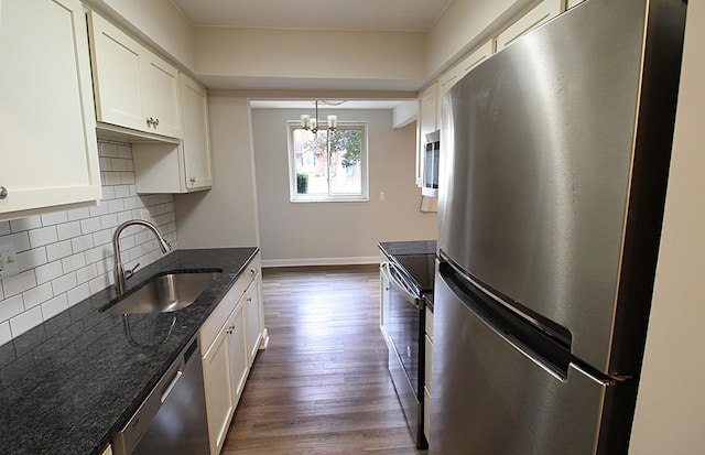 kitchen with white cabinets, appliances with stainless steel finishes, dark stone counters, dark hardwood / wood-style floors, and sink