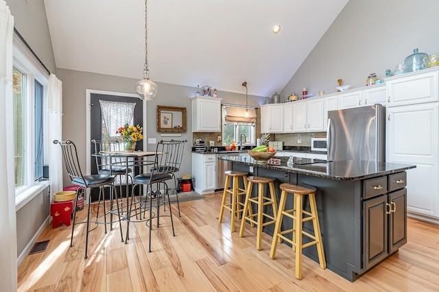 kitchen featuring appliances with stainless steel finishes, a center island, light hardwood / wood-style floors, pendant lighting, and white cabinets