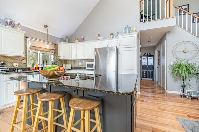 kitchen featuring appliances with stainless steel finishes, white cabinetry, high vaulted ceiling, light wood-type flooring, and dark stone counters