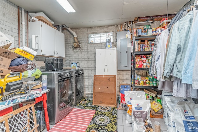 laundry area with brick wall, electric panel, cabinets, and washer and clothes dryer