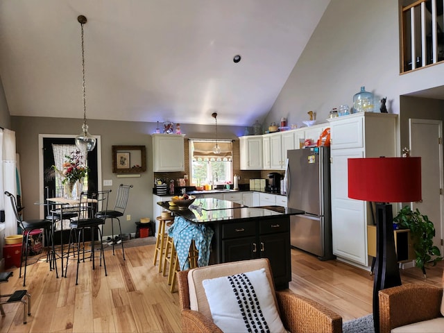 kitchen featuring white cabinets, a kitchen island, light wood-type flooring, stainless steel refrigerator, and pendant lighting