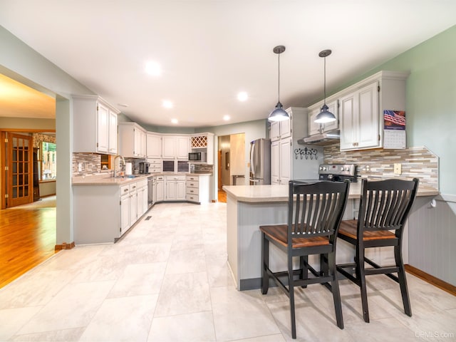 kitchen featuring sink, hanging light fixtures, backsplash, kitchen peninsula, and appliances with stainless steel finishes