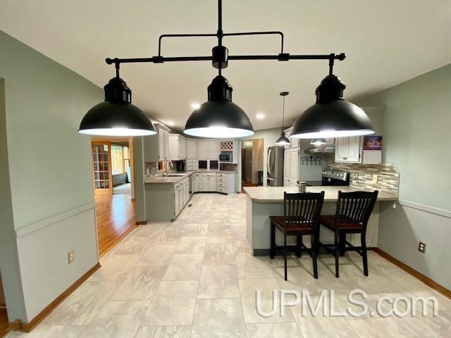 kitchen with a kitchen breakfast bar, decorative backsplash, gray cabinets, appliances with stainless steel finishes, and kitchen peninsula