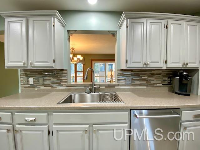 kitchen with decorative backsplash, stainless steel dishwasher, sink, a chandelier, and white cabinetry