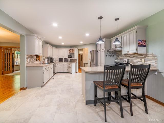 kitchen with sink, appliances with stainless steel finishes, tasteful backsplash, decorative light fixtures, and kitchen peninsula