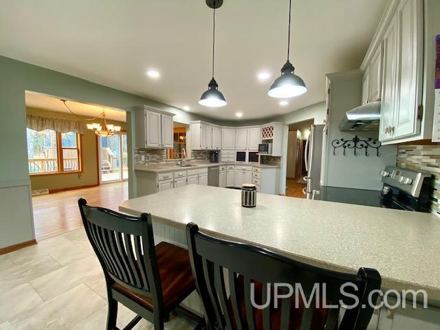 kitchen with white cabinetry, stainless steel appliances, tasteful backsplash, kitchen peninsula, and a chandelier