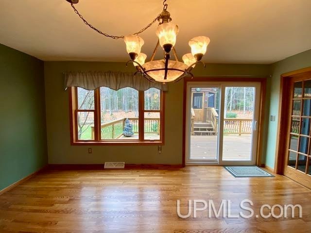 unfurnished dining area with hardwood / wood-style flooring, an inviting chandelier, and plenty of natural light