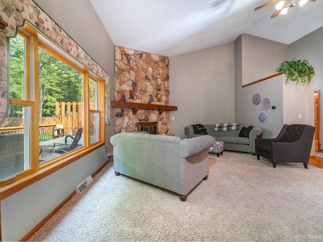 living room with a stone fireplace, ceiling fan, carpet floors, and lofted ceiling