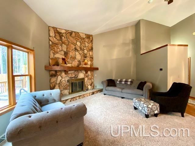 living room with carpet flooring, ceiling fan, a stone fireplace, and lofted ceiling