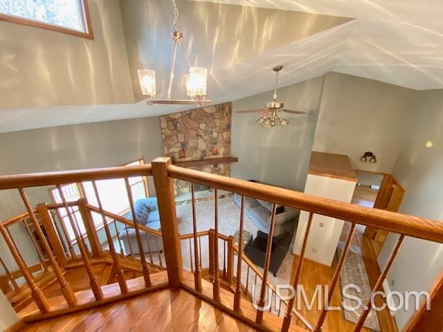 stairway featuring a fireplace, ceiling fan with notable chandelier, hardwood / wood-style flooring, and vaulted ceiling