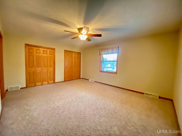 unfurnished bedroom with carpet, ceiling fan, and two closets