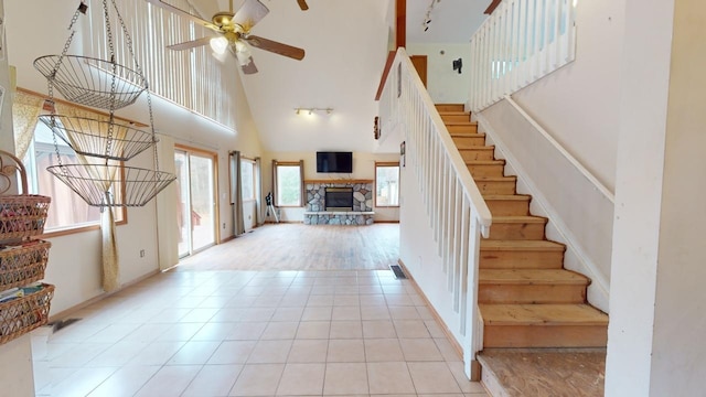 entryway with a fireplace, ceiling fan, light wood-type flooring, and high vaulted ceiling