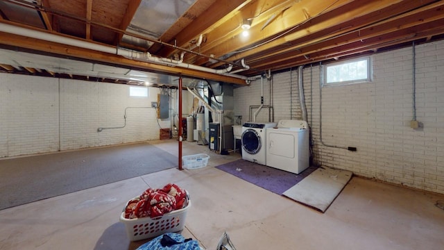 basement featuring water heater, heating unit, washing machine and clothes dryer, and brick wall