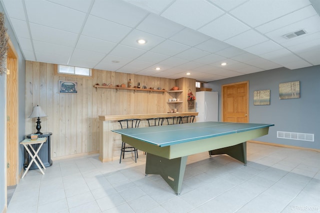 recreation room featuring a paneled ceiling, wooden walls, and light tile patterned floors