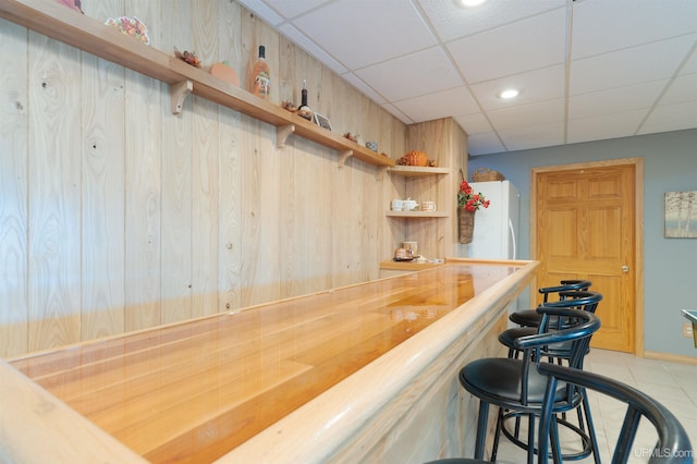 bar with light tile patterned flooring, wood counters, white refrigerator, and a drop ceiling