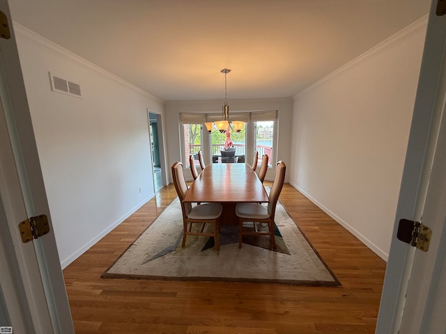 dining space featuring dark wood-type flooring, crown molding, and an inviting chandelier