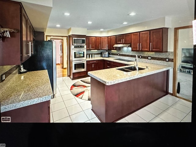 kitchen with appliances with stainless steel finishes, light tile patterned floors, sink, a kitchen breakfast bar, and kitchen peninsula