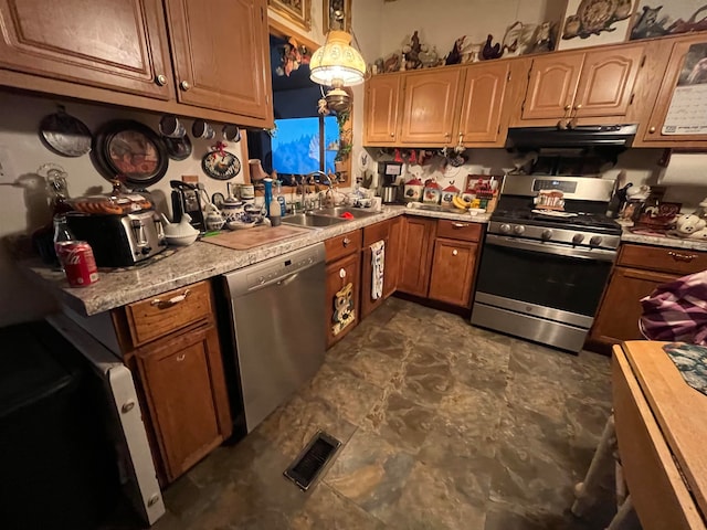 kitchen with appliances with stainless steel finishes, decorative light fixtures, sink, and range hood