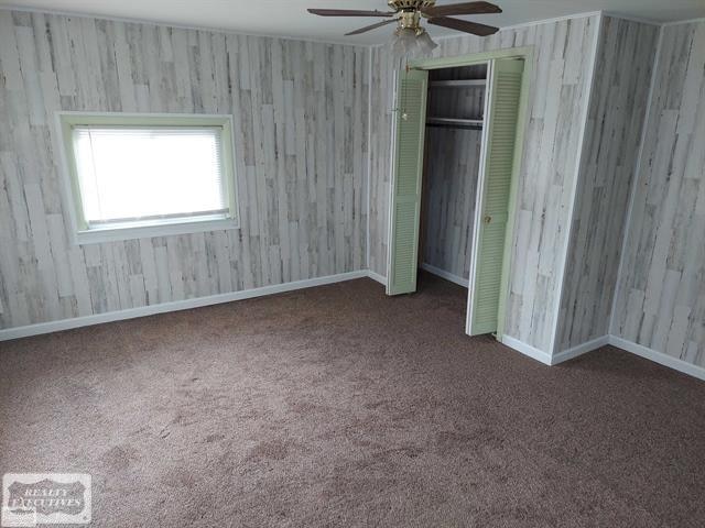 unfurnished bedroom with dark colored carpet, ceiling fan, and a closet