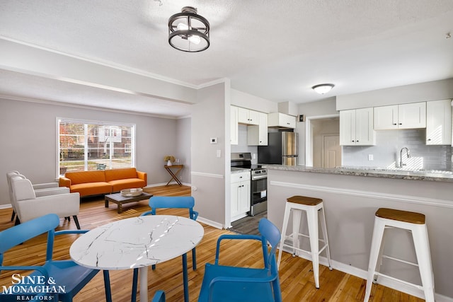 kitchen with stainless steel appliances, backsplash, light stone countertops, white cabinetry, and light wood-type flooring