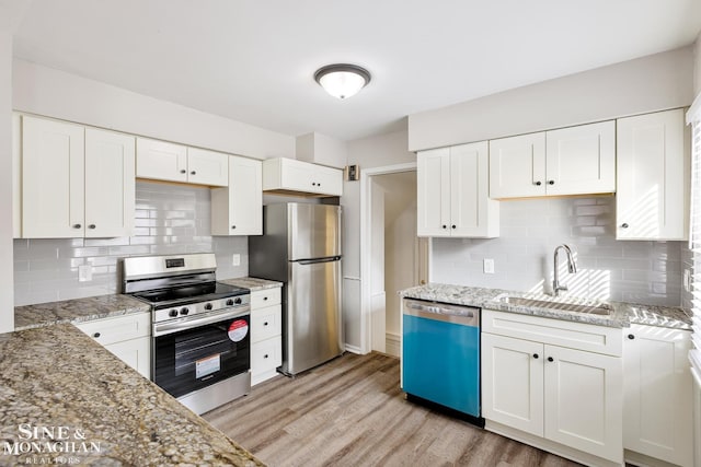 kitchen with light hardwood / wood-style floors, stainless steel appliances, sink, tasteful backsplash, and white cabinetry