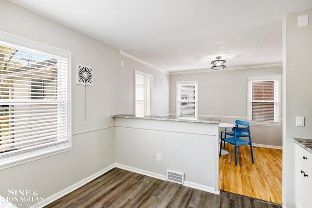 kitchen with white cabinetry, light stone counters, kitchen peninsula, ornamental molding, and dark wood-type flooring