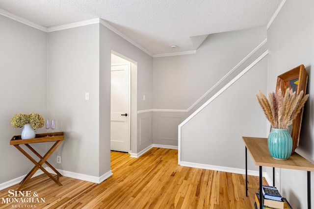 corridor with light hardwood / wood-style flooring, a textured ceiling, and crown molding