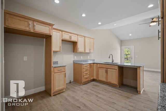 kitchen featuring light wood-style flooring, a sink, light stone countertops, vaulted ceiling, and a peninsula