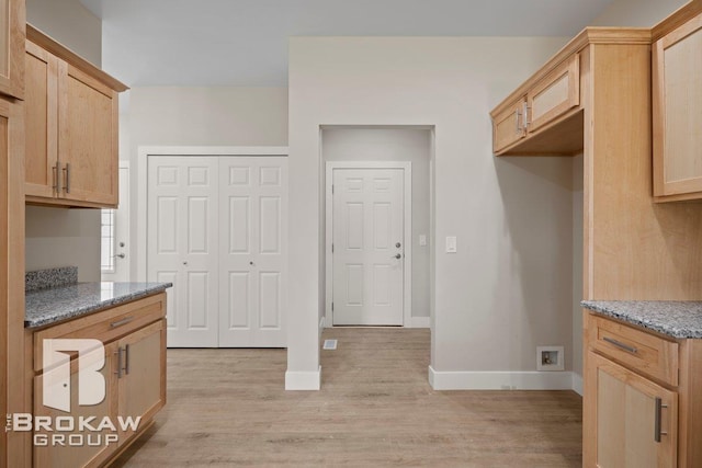 kitchen with light brown cabinetry, light stone counters, light wood-style flooring, and baseboards