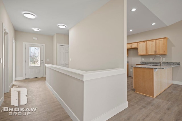 kitchen featuring light brown cabinetry, baseboards, light wood-style flooring, and a sink