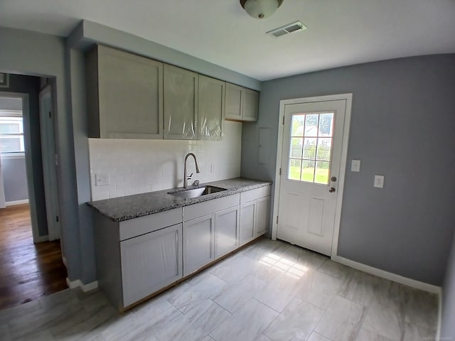 kitchen featuring dark stone countertops, tasteful backsplash, sink, and a healthy amount of sunlight