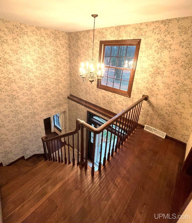 stairs with hardwood / wood-style flooring and an inviting chandelier