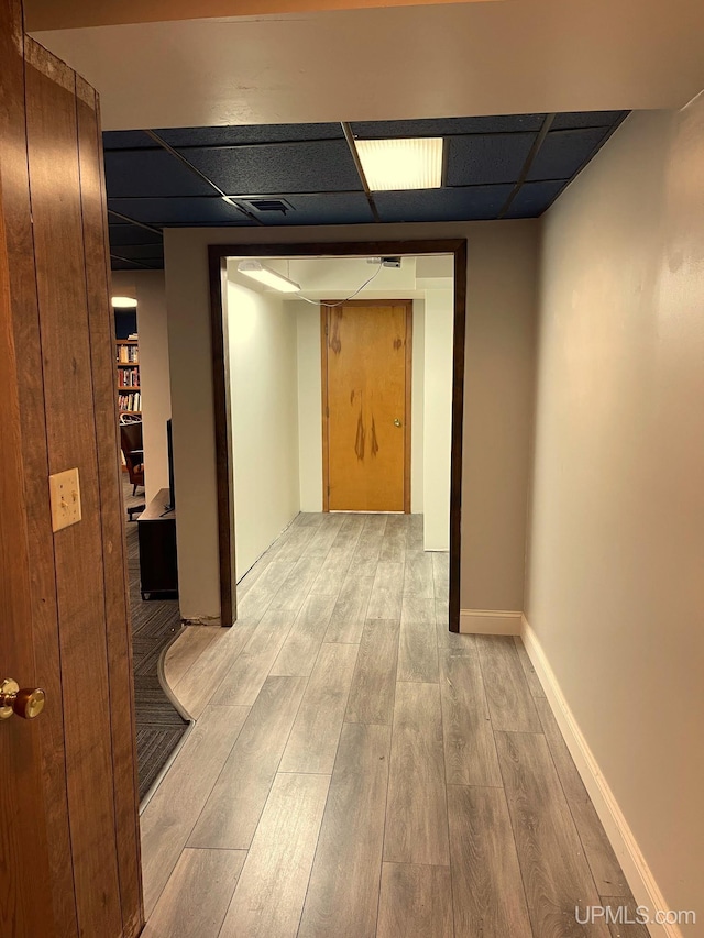 corridor with a paneled ceiling and light hardwood / wood-style flooring