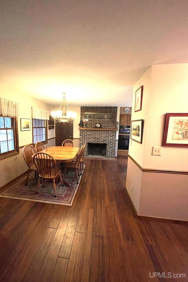 dining room with dark hardwood / wood-style floors, an inviting chandelier, and a brick fireplace