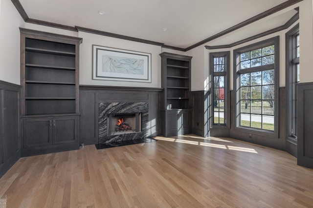 unfurnished living room featuring a healthy amount of sunlight, crown molding, a fireplace, and light hardwood / wood-style flooring