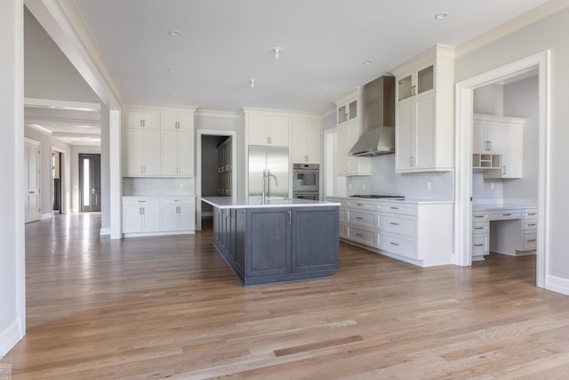 kitchen featuring a center island with sink, white cabinets, and wall chimney range hood